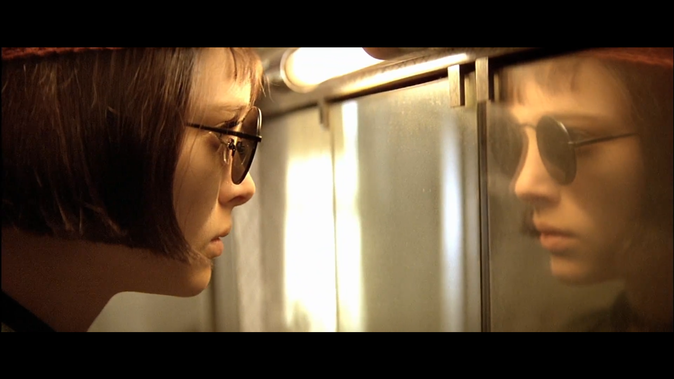 Mathilda, wearing glasses, looks at her own reflection.