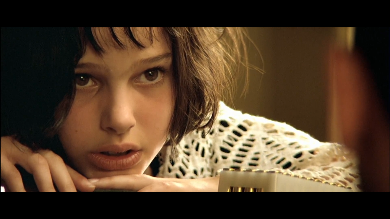 Mathilda leans forward on the table, resting her chin on a handgun.